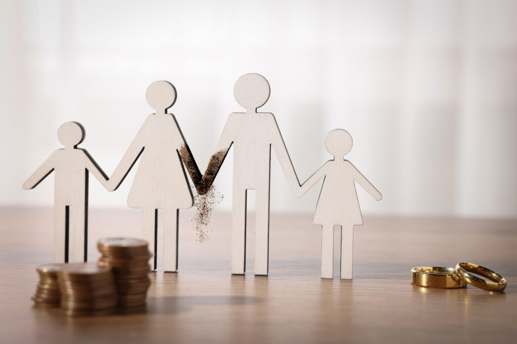 Figuras de madera de una familia separada con monedas y anillos, representando divorcio, custodia y pensión de alimentos en Castellón
